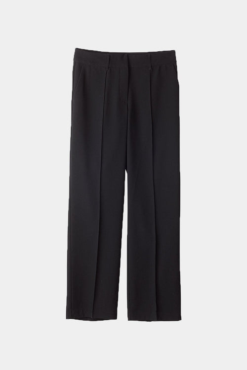 A model wearing black wide-leg pleated trousers with a white sleeveless top, standing against a plain white studio background.