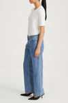 Person wearing a white top and blue jeans on a plain background